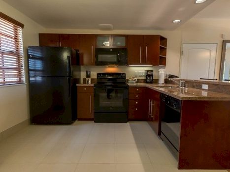 A modern kitchen with dark wood cabinets, a black fridge, black stove, microwave, and a central island with a sink, under bright overhead lights.
