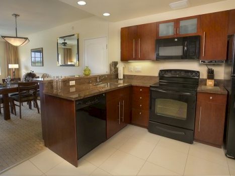 A modern kitchen with dark wood cabinets, black appliances, a breakfast bar, and open dining area in the background.