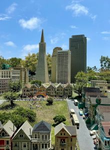 A cityscape with a central park, a tall modern tower, lush greenery, and surrounding low-rise buildings under a sunny blue sky.