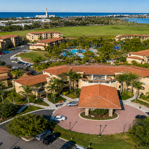 Aerial view of a campus or complex with a central circular plaza, red-roofed buildings, greenery, parking lots, and surrounding roads.