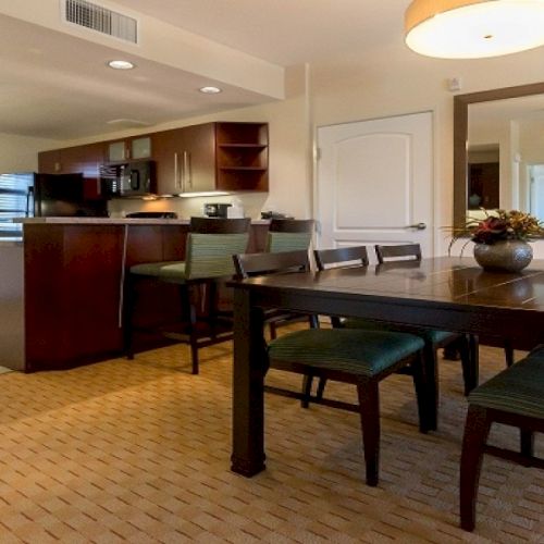 A cozy dining area and living room with a dark wood table, black chairs, and warm lighting in a homey open-plan space.