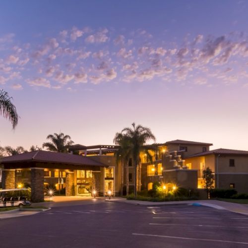 A luxurious hotel entrance at dusk, with palm trees, warm lights, and a grand driveway. Top it at 140 characters, always ending the sentence.