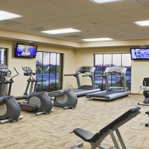 A busy gym with various cardio and weight machines, mirrors, and a few people working out in a bright, modern facility.